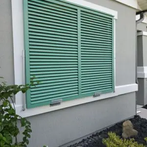 Green louvered shutters on gray house exterior.