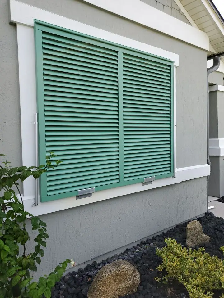 Green louvered shutters on gray house exterior.