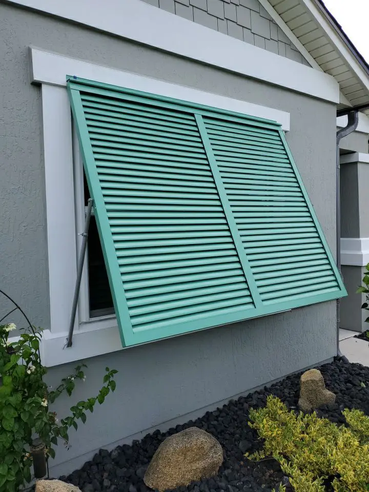 Turquoise louvered window awning on house.